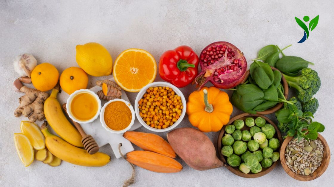Top 10 Indian foods to boost immunity shown, including citrus fruits, turmeric, ginger, garlic, banana, sweet potato, pumpkin, pomegranate, spinach, broccoli, mint, brussels sprouts, seeds, honey, and red bell pepper arranged on a light surface.